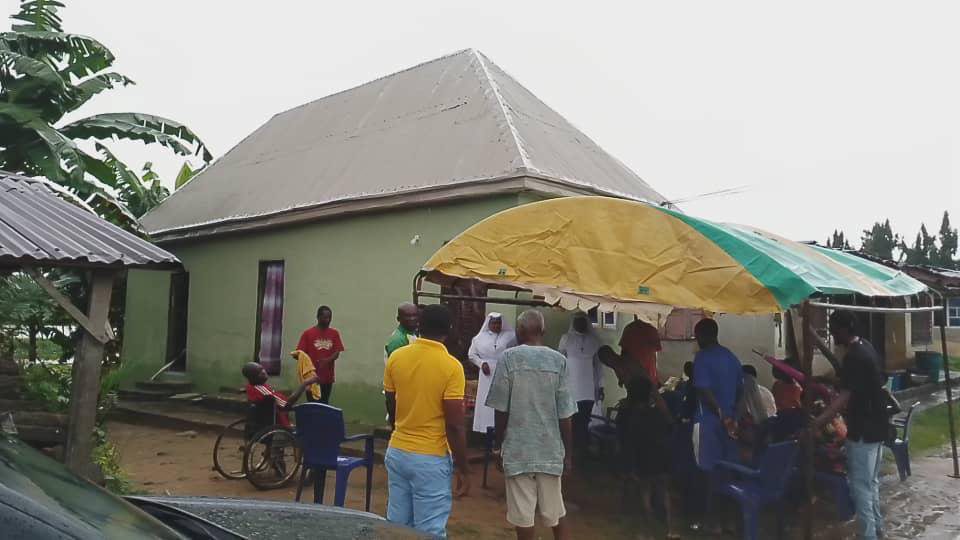Group of people gathered outside a green house with a canopy tent.