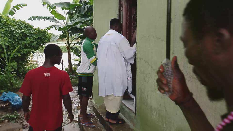 Man in white robe entering a green building with others nearby.