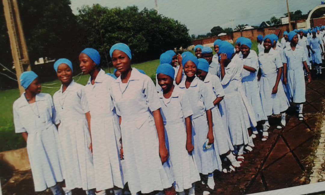 Nurses in white uniforms and blue caps standing in a line outdoors.