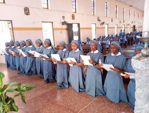 Nuns in blue habits stand in a church holding lit candles.