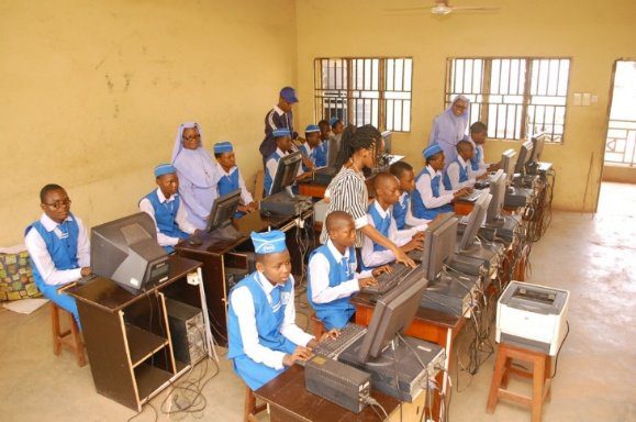 Students in blue uniforms learning computer skills in a classroom.