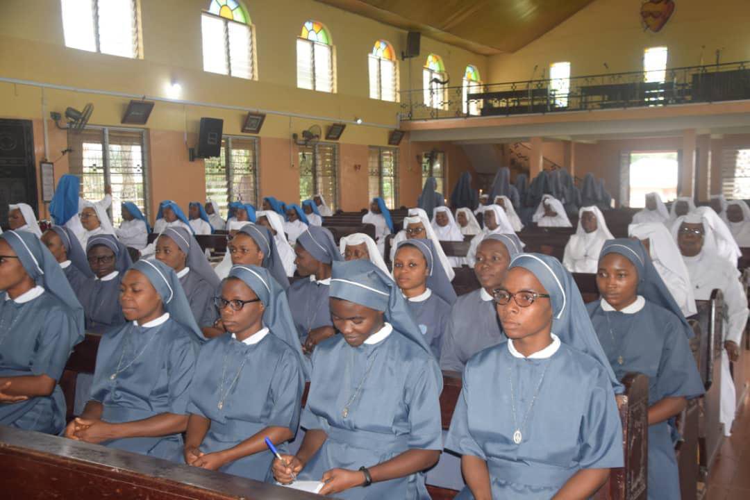 Group of nuns seated in a church or chapel, dressed in gray habits.