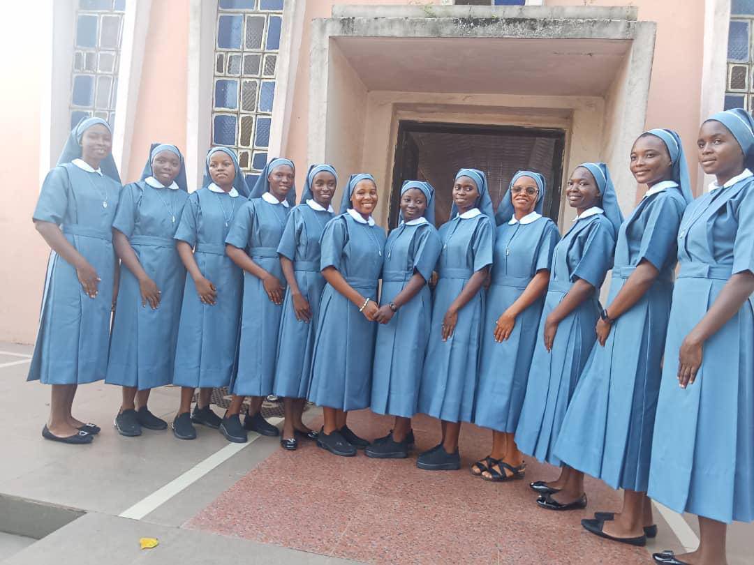 Group of nuns in blue habits standing outside a building.