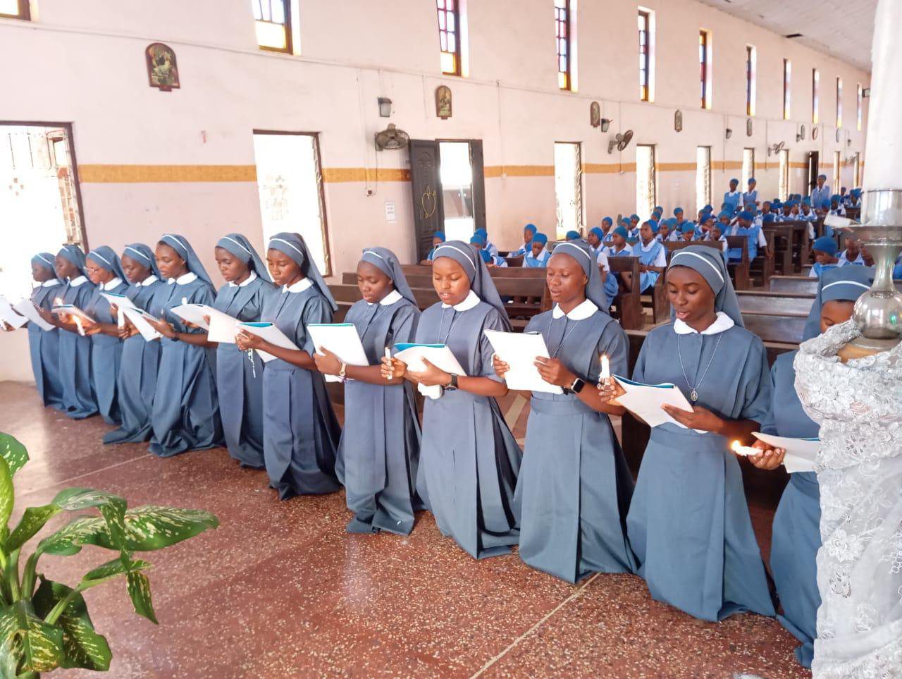 Nuns in blue habits singing together inside a church.