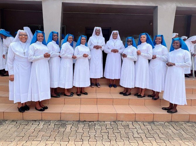 A group of nuns in white habits and blue veils standing together outside.